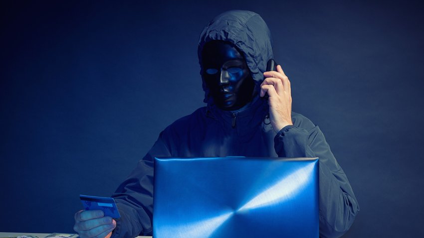 Anonymous hacker in mask programmer uses a laptop to hack the system in the dark. The concept of cybercrime theft of money from bank cards